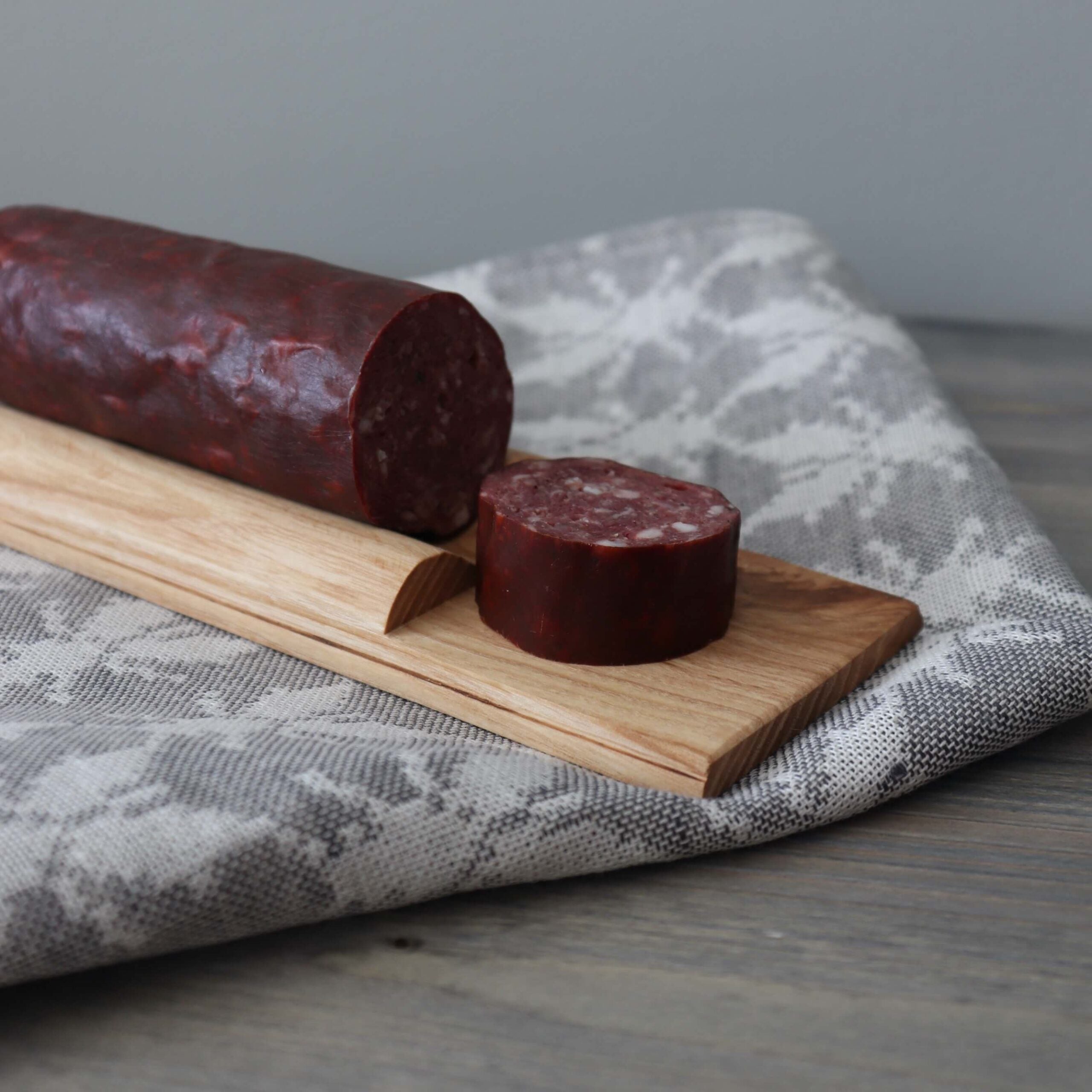 Wooden cutting board with sliced sausage on a linen cloth