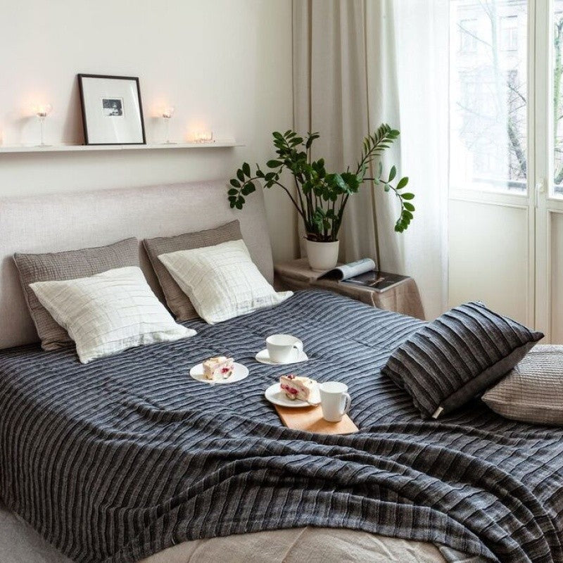 Dark bedcover styled on a bed in a light bedroom interior