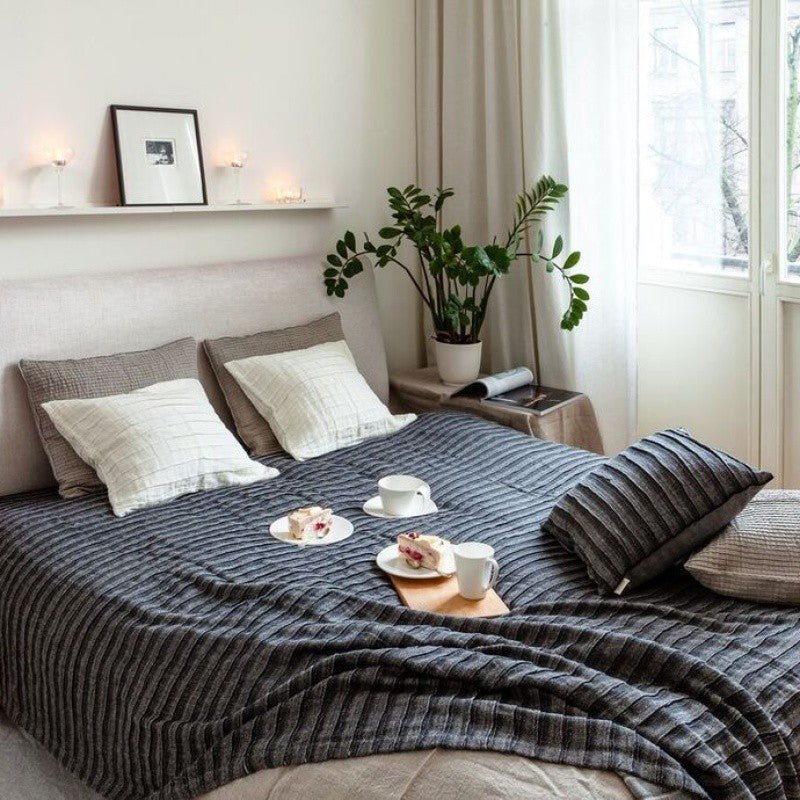 Dark bedcover styled on a bed in a light bedroom interior