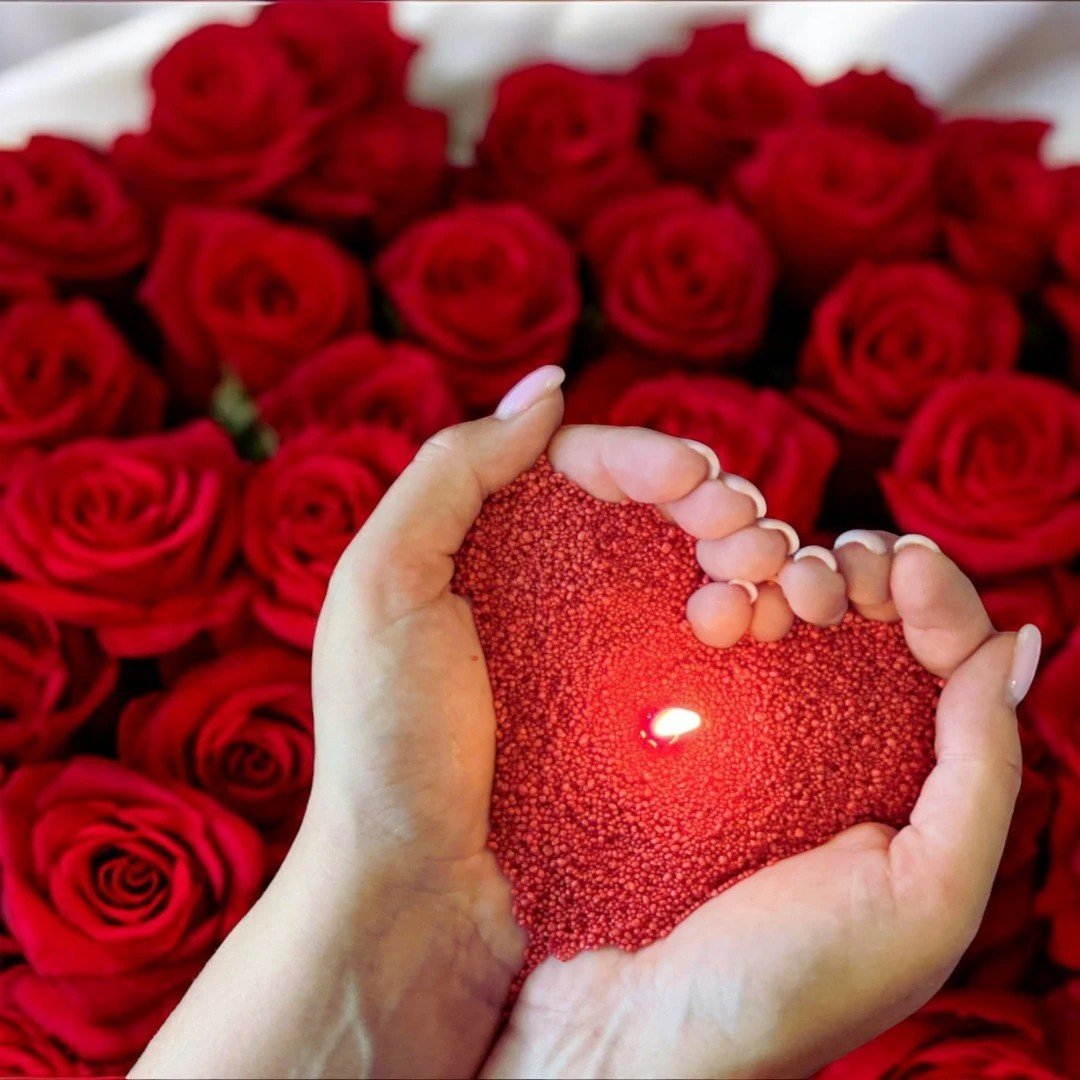 Hands holding glowing red candle sand against a background of red roses