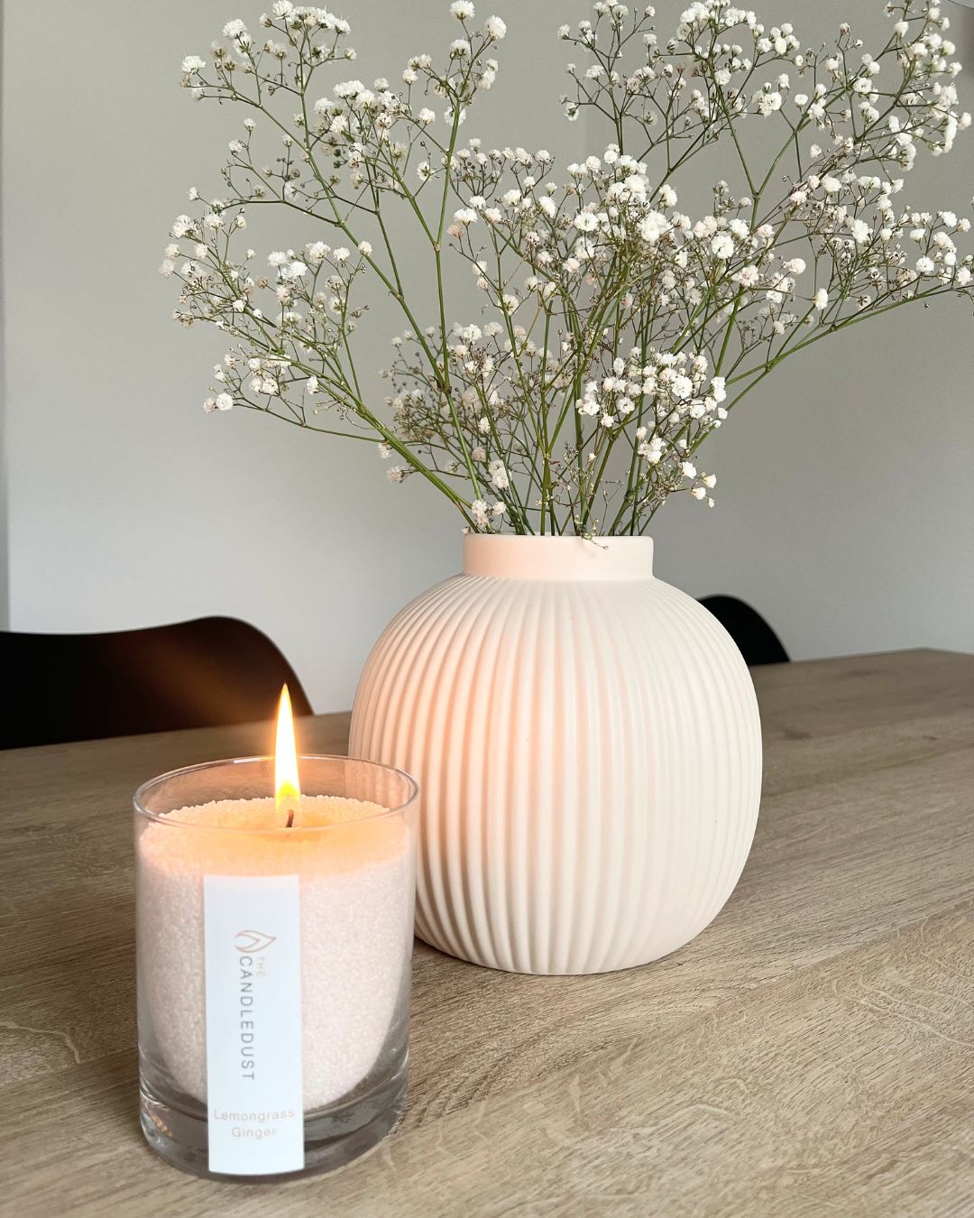 Candledust scented candle in a glass jar beside a ceramic vase with baby's breath flowers