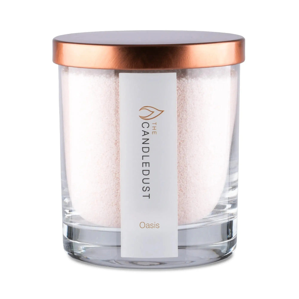 A glass jar candle with white wax, a metallic rose gold lid, and a white label reading 'THE CANDLEDUST' and 'Oasis'.